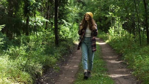 Happy Young Woman with Backpack Walks Along Ground Road in Forest