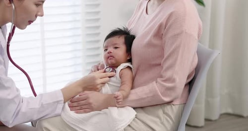 Close-up view of pediatrician examining baby boy’s chest with stethoscope while Asian mother holds