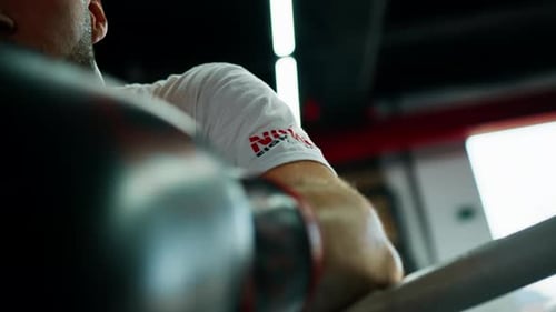 Tired male boxer wearing boxing gloves rests near the arena