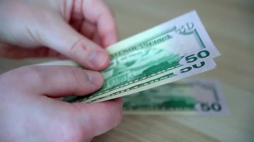 Hands Counting Fifty Dollar Bills on Table