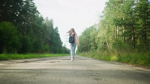 Back View of Woman Walking Alone on Forest Road Carrying Backpack