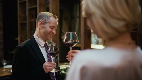 Couple d'âge moyen faisant tinter des verres à vin dans un restaurant de luxe