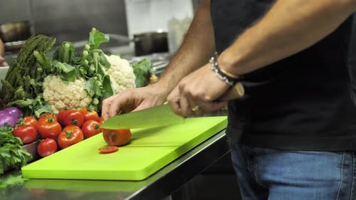 Unrecognizable chef slicing red tomato on cutting board in restaurant kitchen