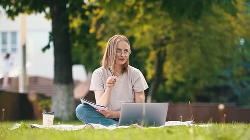 On the grass with laptop. Beautiful female student is outdoors near the university.