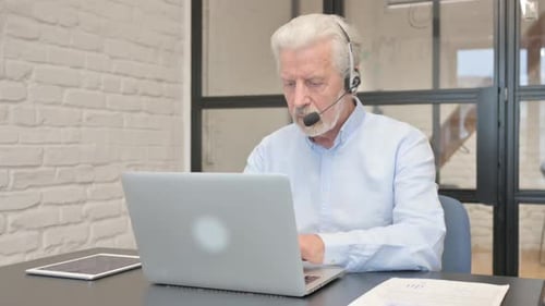 Senior Man with Headset Working on Laptop in Call Center