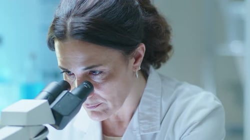 Woman Looks Through a Microscope in Laboratory