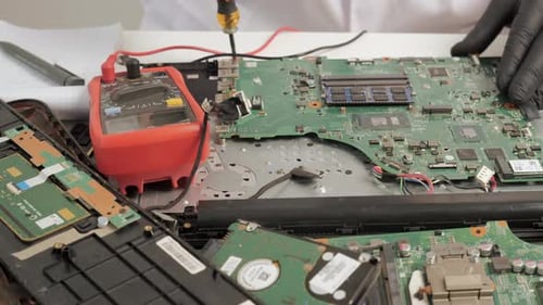 Primer plano de la reparación de la placa base de una computadora portátil con multímetro y herramientas