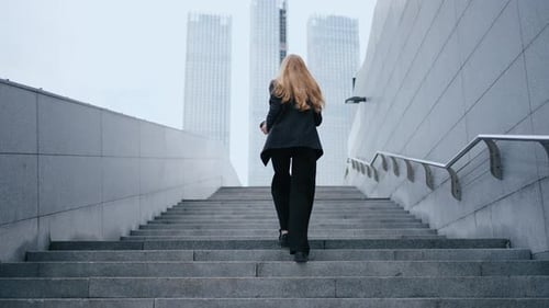 View From the Back of a Business Woman Climbing Stairs in a Modern City Against the Backdrop of City