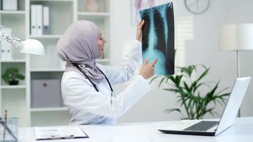 Confident muslim female doctor examining x-ray picture while sitting at workplace in office in hospi