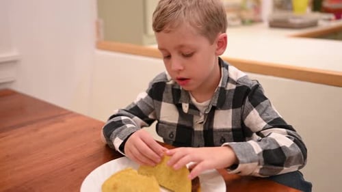 Young Boy Enjoying Tacos at Table Indoors