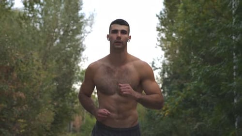 Handsome Muscular Sportsman with Wireless Headphones Running Along Road with Beautiful Nature