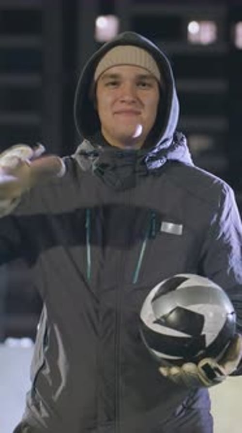 Smiling Man in Hoodie Hitting Soccer Ball on Urban Field at Night