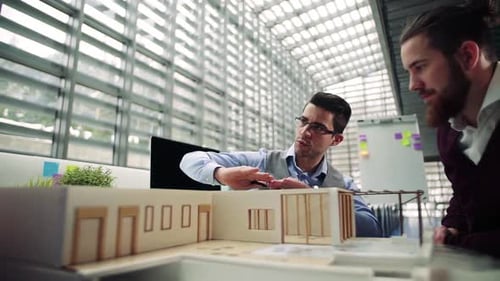 Two Young Architects with Model of a House in Office, Talking