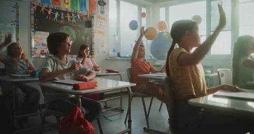 Elementary School Students Sitting at the Desks Raising Hands to Provide Correct Answer