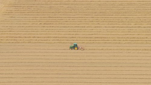 Aerial pass over tractor plowing farmland with farm buildings, Netherlands
