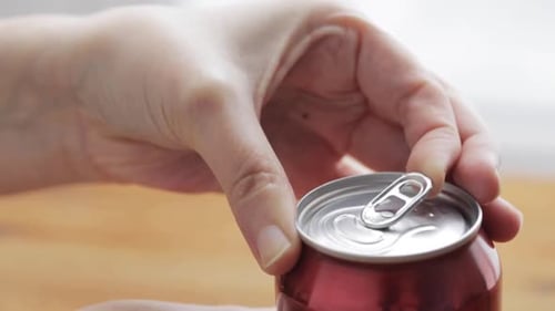 Hand opens a red can of soda