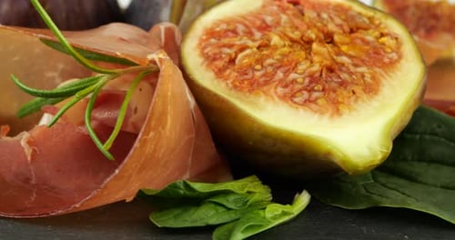 Figues, jamon et feuilles d'épinards sur une planche de service en pierre noire. Set de snacks.