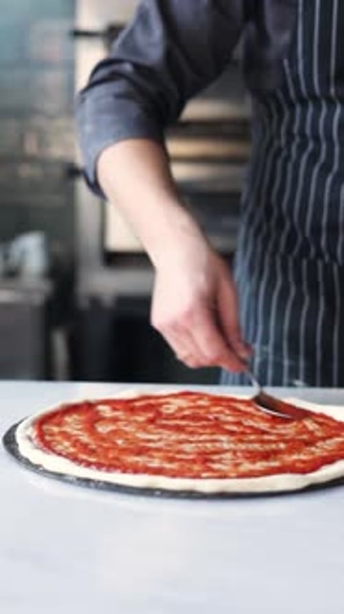 Le chef étale la sauce tomate sur la pâte à pizza