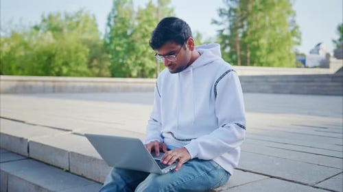Young Adult Working on Laptop Outdoors in Urban Setting