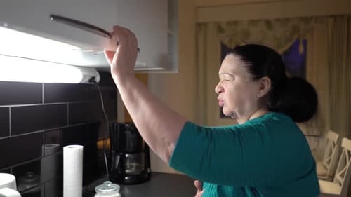 Senior Woman Taking Pills in Kitchen with Water