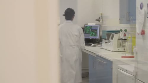 Female Scientist walks into science laboratory and looks at screen with stem cells