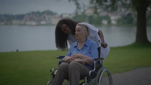 Caregiver Pushing Senior Woman in Wheelchair Outdoors