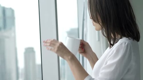 Young Businesswoman Drinking Coffee and Admire View From Window at Office 30s