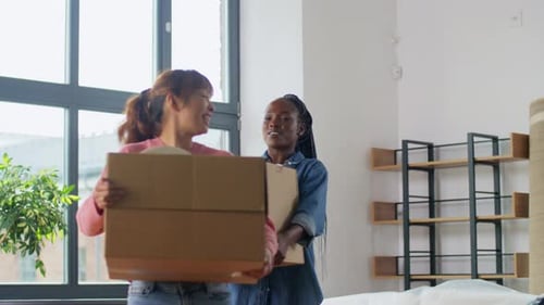 Two Smiling Women Carry Boxes Into New Home