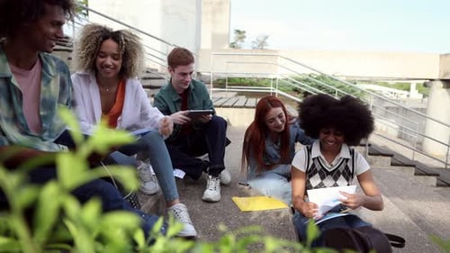 Group of cheerful young multiracial college students sitting on the stairs in front of the campus bu