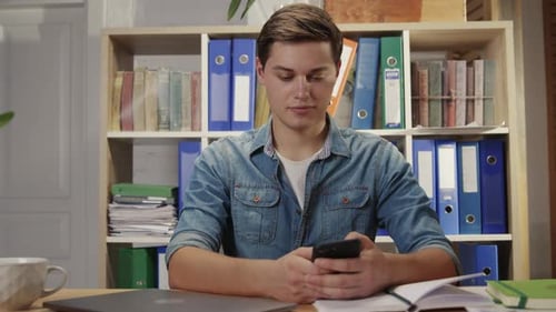Young Man Using Smartphone at Desk Indoors