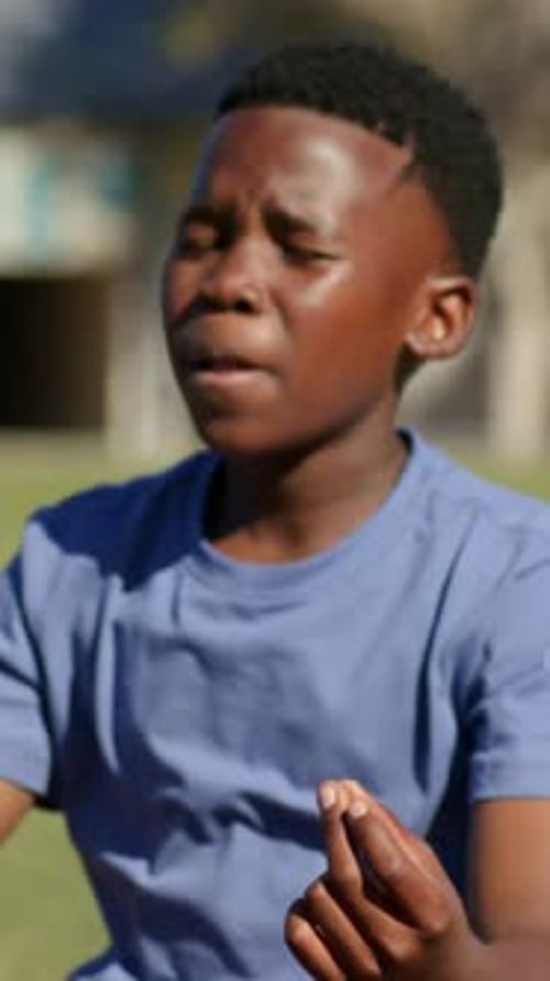Vertical video: Holding pinch after tongue out, teen holding breath to focus at park, blue tee