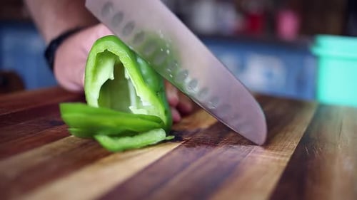 Green bell pepper is sliced on wooden cutting board, low angle closeup