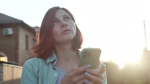 30s Woman Holding Cell Phone in Hands Standing on the Street