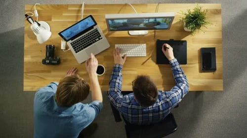 Top View of Two Young Talented Photographers Discussing Footage. One of Them Works on a Digital Dra