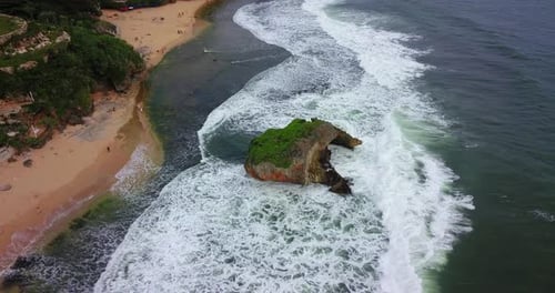 Vue aérienne des vagues à calotte blanche qui se forment au-dessus d'un récif corallien et s'écrasent sur la plage de Ngandong