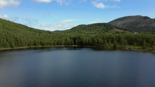 Aerial over Nisser lake towards a forest with the Langfjell Mountain range in the background, Treung
