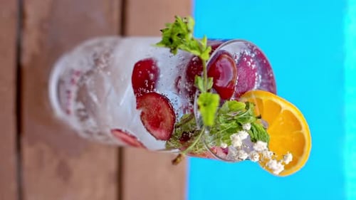 Mojito cocktail glass with ice and cherry and mint, soda and gin near a blue pool close up