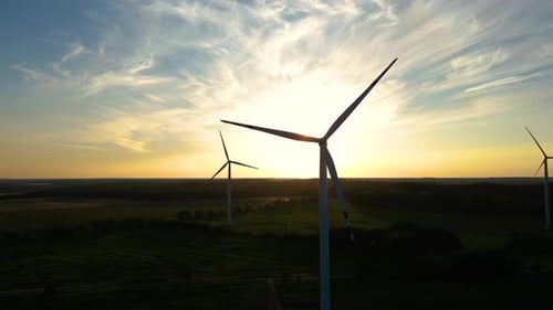 Large wind turbines with blades in field aerial view bright orange sunset blue sky wind park slow mo
