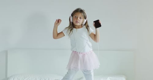 Happy Little Girl Dancing to Music on Bed