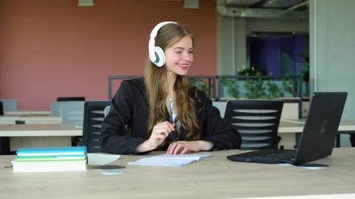 Smiling Girl with Headset Studying Online Using Laptop at University Taking Notes Copy Space