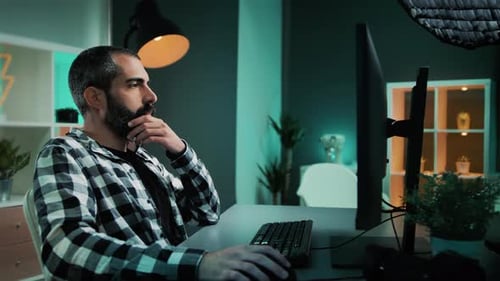 Editor, freelancer or designer with beard sitting on desk using desktop computer keyboard and mouse.