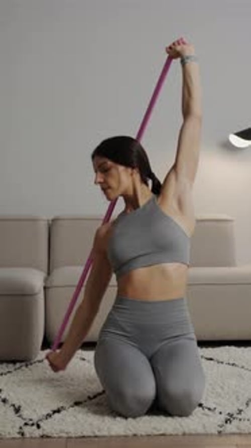 Focused Woman Performing Resistance Band Shoulder Workout at Home Kneeling on Soft Carpet in Modern