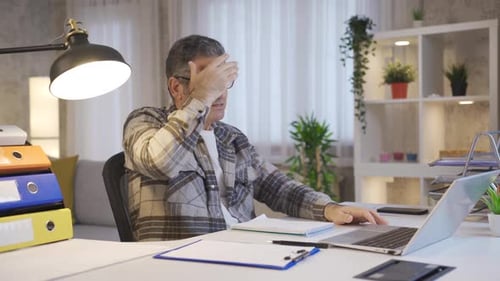 Stressed and sad mature man with laptop working in Home Office.