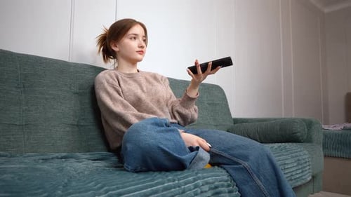Young Woman Sits with Remote Control on Couch