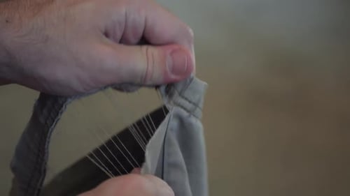Hand Tearing Worn Fabric Showing Ripped Clothing Seam Close-Up