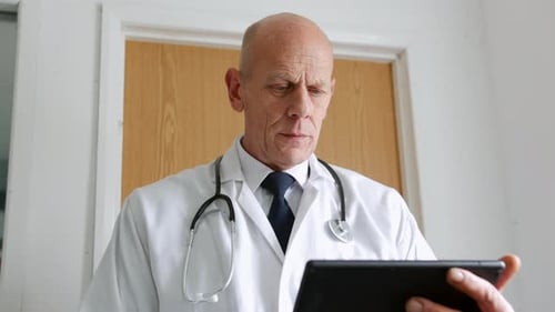 Close up of a mature doctor using a tablet computer in a hospital. The unrecognizable man is standin