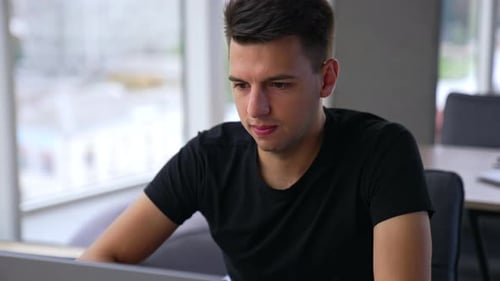 Busy young focused man working on laptop. Brunet male employee concentrated on the office work.