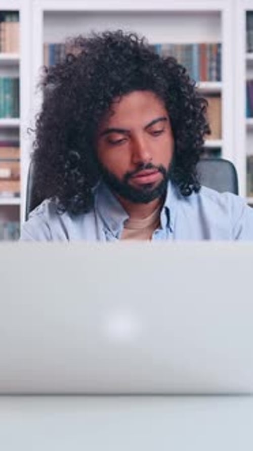 Focused Man Working on a Laptop in a Serene Library Setting