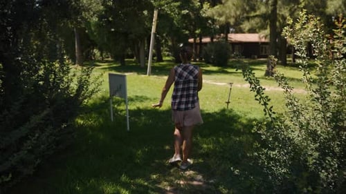 Mulher estende os braços enquanto caminha por um caminho estreito cercado por vegetação densa e árvores