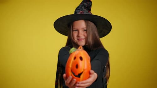 Girl Dressed as Witch Holds Halloween Pumpkin Decoration